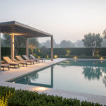 Les 8 équipements à prévoir pour créer un espace piscine agréable et pratique Espace piscine élégant au coucher du soleil, avec transats sous une pergola, éclairage doux et terrasse soignée dans un jardin contemporain.