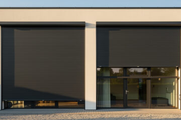 Façade de maison contemporaine avec volets roulants gris anthracite fermés, éclairage chaud d’été et rendu architectural soigné.