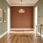 Quelle peinture choisir pour donner du style à un couloir ? Couloir élégant aux murs vert sauge avec un mur d’accent terracotta, des boiseries blanches et un sol en chêne clair.