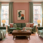 Quels codes déco choisir pour une maison new-yorkaise façon Wes Anderson ? Salon d'une maison new-yorkaise aux murs rose poudré et vert céladon, avec un canapé en velours et du mobilier en noyer disposés symétriquement sous une lumière douce.